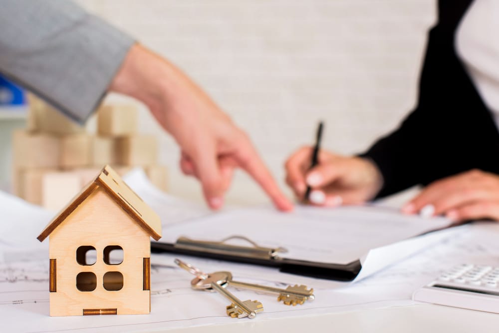 Wooden house model with keys and two people reviewing documents on a desk