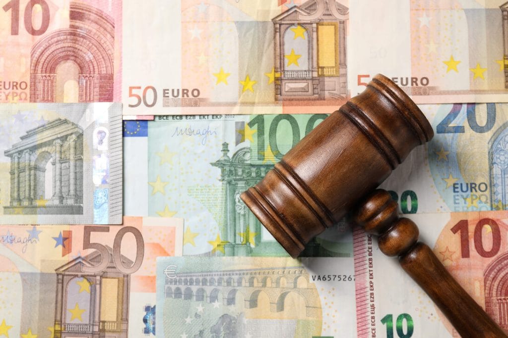 Wooden gavel resting on a spread of euro banknotes, symbolizing a financial or legal judgement.
